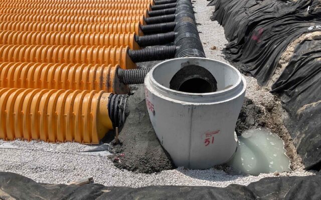 Yellow drainage pipes connect to a concrete manhole on gravel.