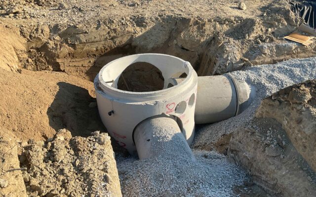 Concrete storm drain manhole sits in open trench amid dirt.