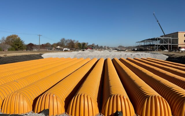 Orange drainage pipes on gravel at a construction site.