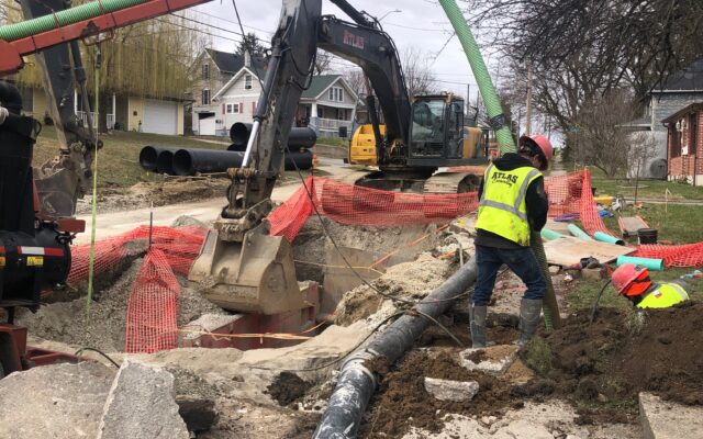 Workers use excavators and hoses on a large underground pipe.