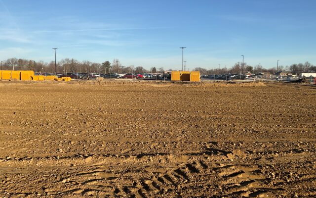 Large flat construction site with dirt, tire tracks, equipment, cars.
