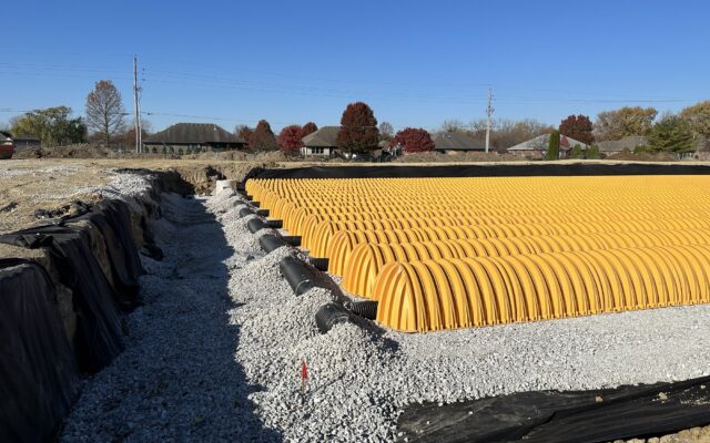 Rows of yellow stormwater chambers on gravel at a construction site.
