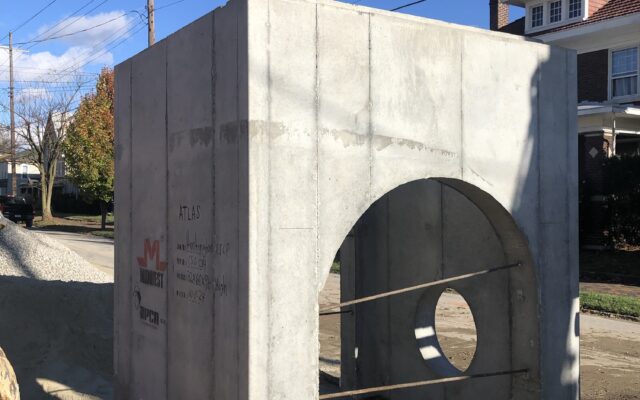 Concrete box with round holes on dirt site near houses.