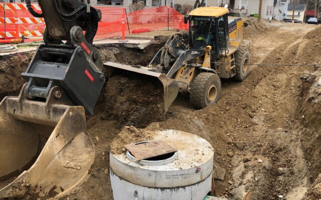 Excavator and loader working by concrete pipes on a street.