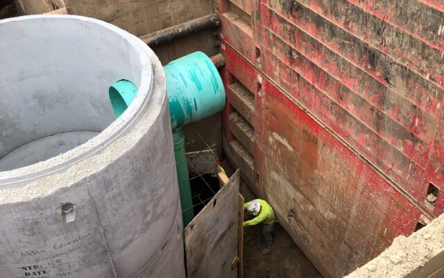 Worker in trench beside concrete pipe and green utility pipe.
