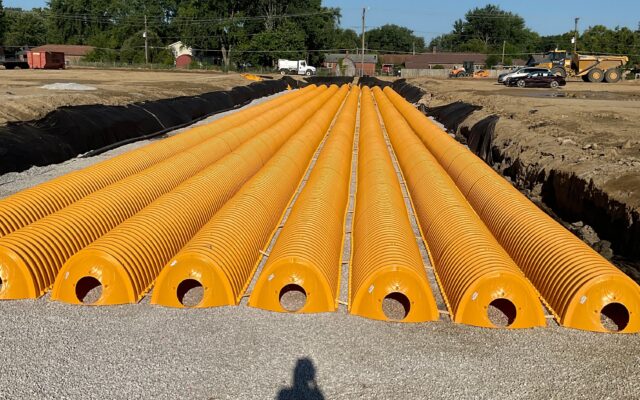 Yellow drainage pipes lined up in a trench at construction site.