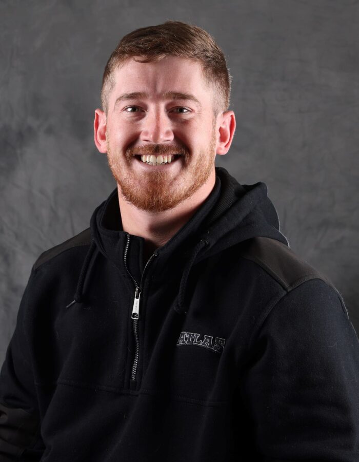 Man with short brown hair and beard smiles in black hoodie.