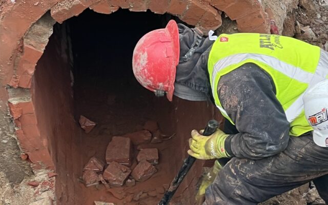 Worker in vest and red helmet clears debris at brick tunnel.