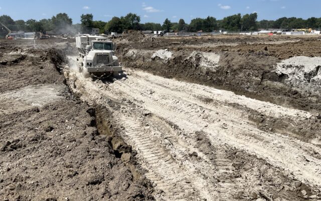Dump truck drives through muddy trench at construction site.