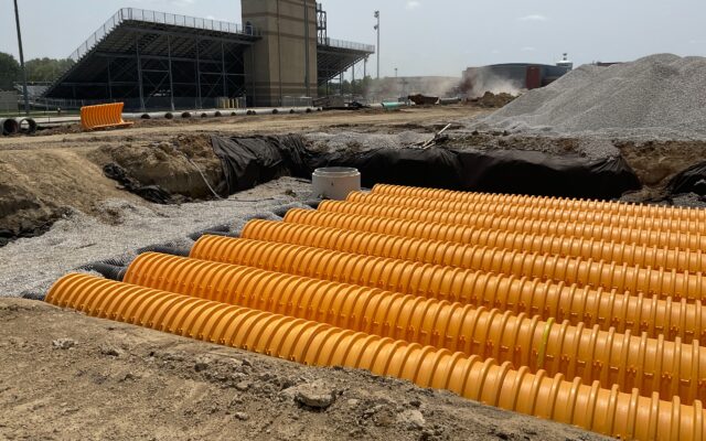 Yellow drainage pipes line a construction site near stadium.