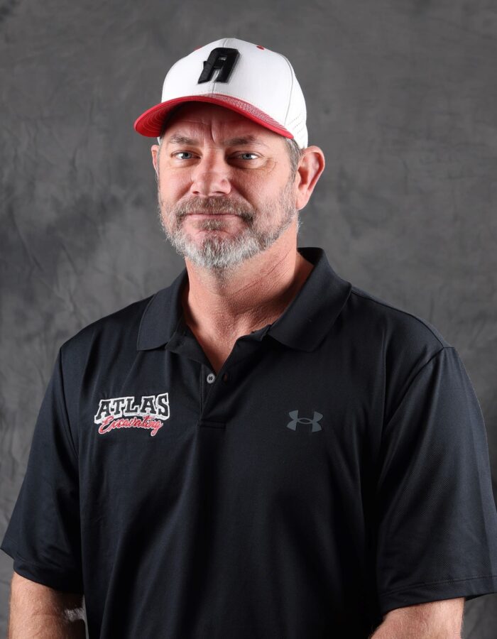Bearded man in cap and Atlas polo stands by gray backdrop.