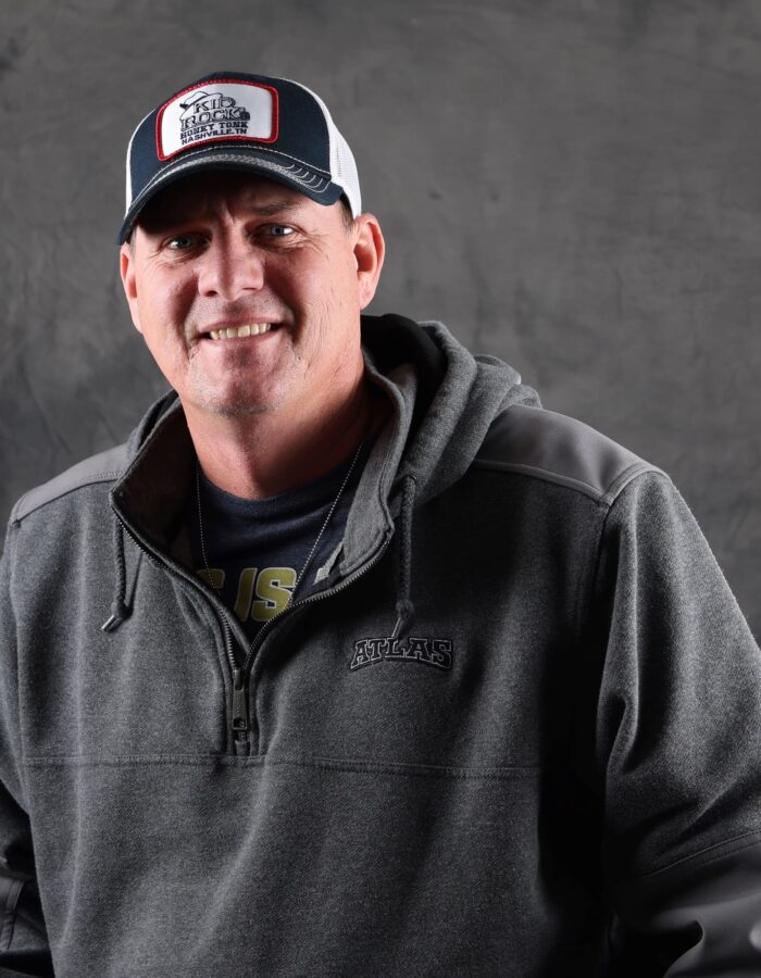 Man in gray hoodie and hat smiles at camera.