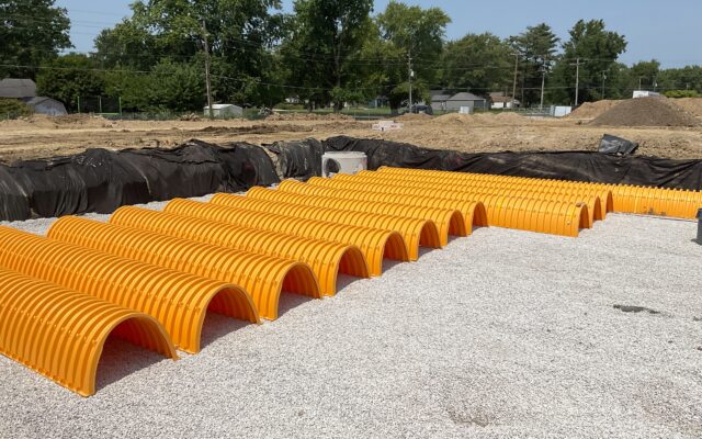 Yellow plastic stormwater chambers on gravel, with dirt and trees.