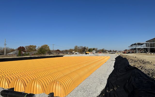 Rows of yellow stormwater chambers on gravel, clear sky above.
