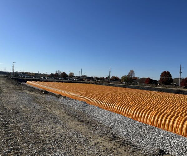 Orange stormwater chambers lined up on gravel at construction site.