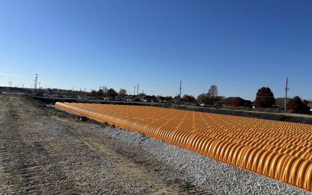 Orange stormwater chambers lined up on gravel at construction site.
