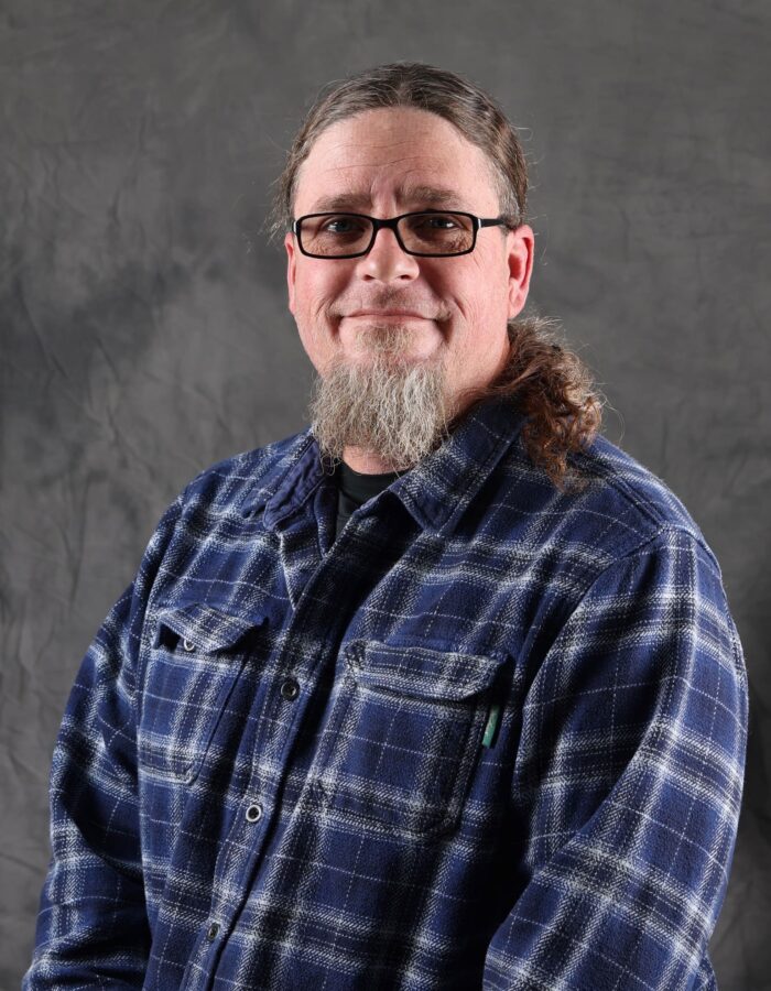 Person with glasses, long beard and hair, blue plaid shirt.