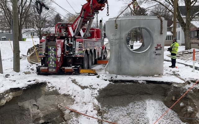 Crane lifts concrete above snowy site; worker watches.