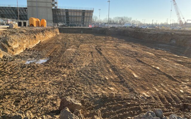 Excavation site with equipment and stadium under clear sky.