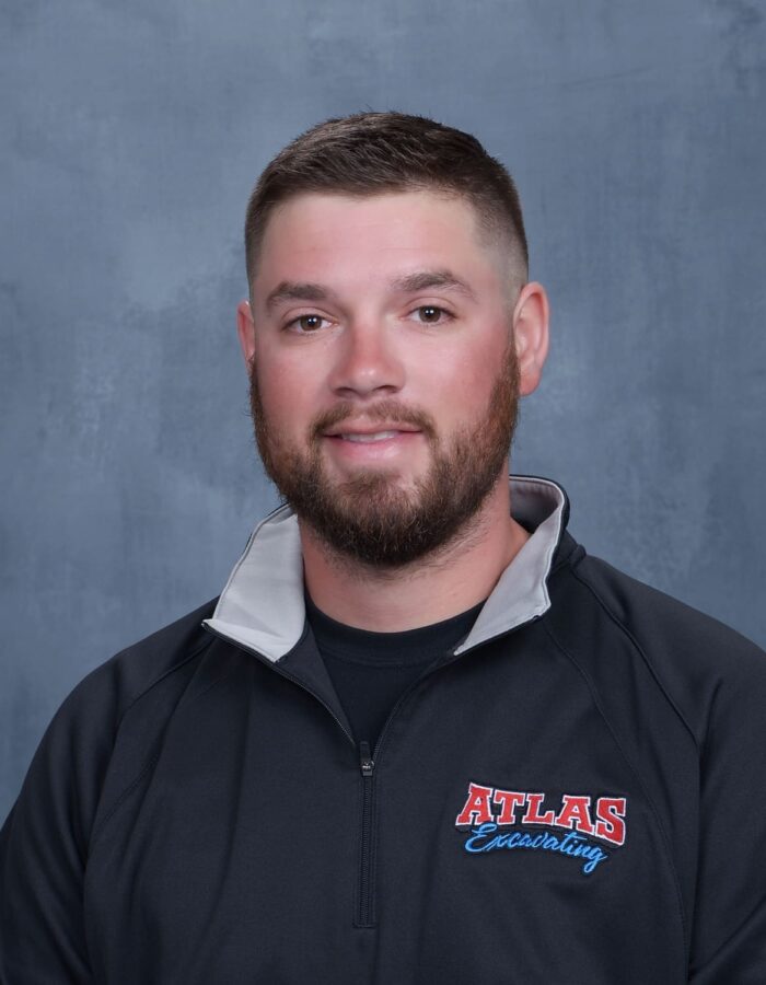 Man with short brown hair, beard, black Atlas jacket, gray backdrop.