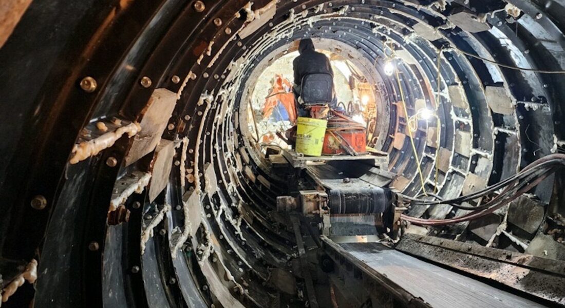 Worker in a lit, metal-lined tunnel under construction.