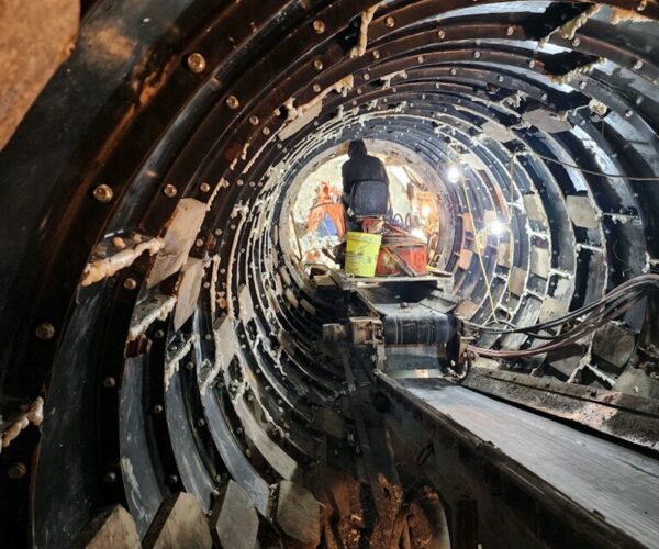 Worker in a lit, metal-lined tunnel under construction.