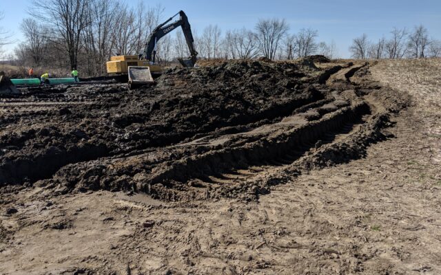 Excavator and workers at muddy site with deep tracks.