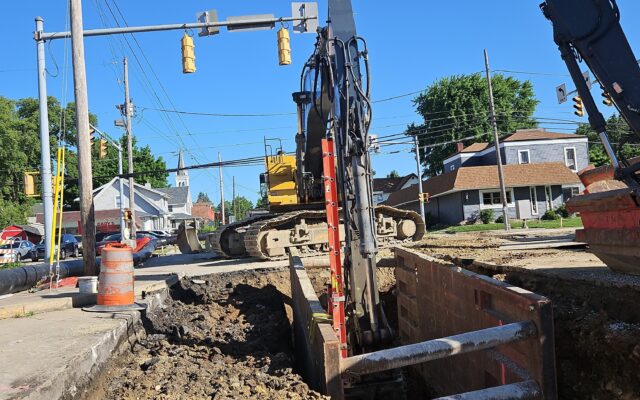 Excavators and traffic lights at city street construction site, trenches visible.