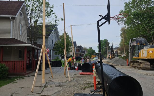 Workers install black pipes on street with cones and equipment.