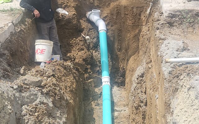 Worker in hard hat beside large blue pipe in trench.
