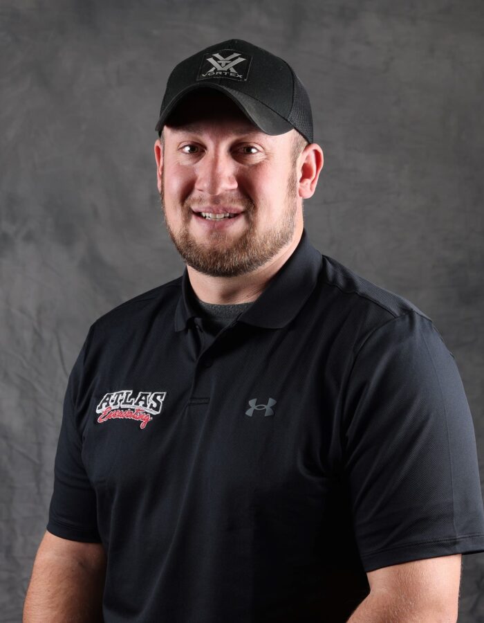 Man in black Atlas cap and polo poses by gray backdrop.