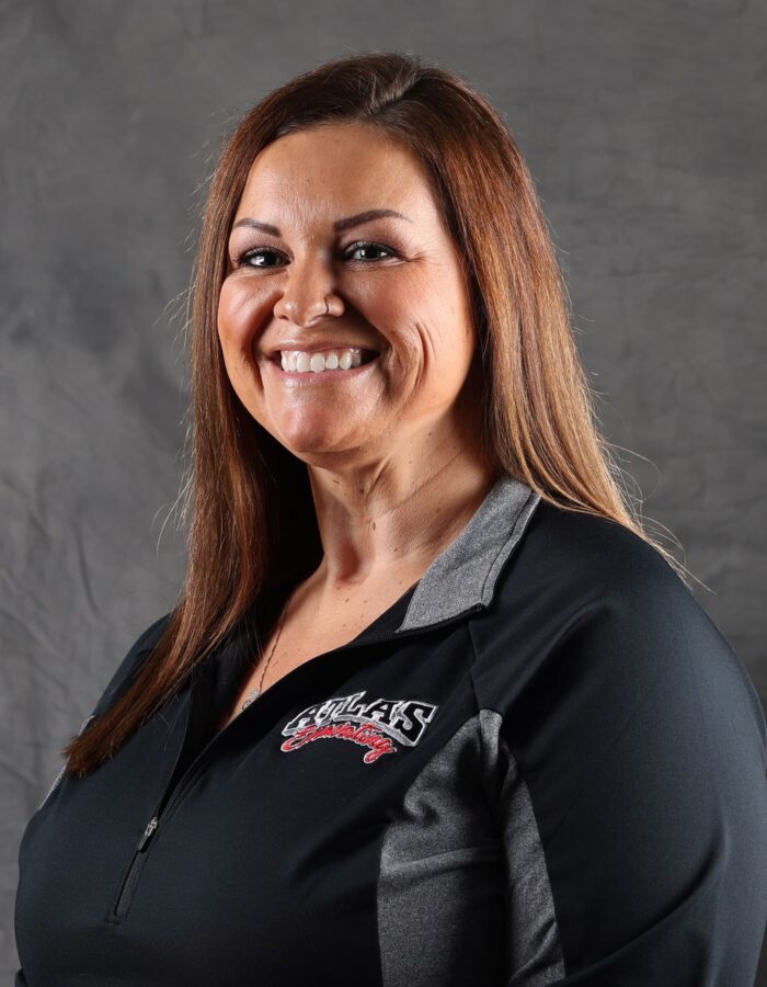 Smiling woman with straight brown hair in logo zip-up shirt.