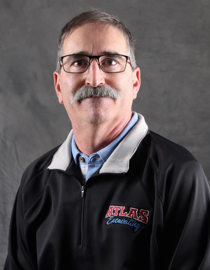 Man with glasses and mustache in black jacket, posing.