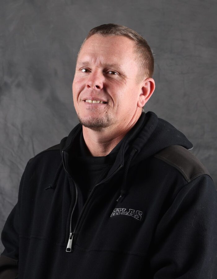Man in black hoodie smiles before a gray backdrop.