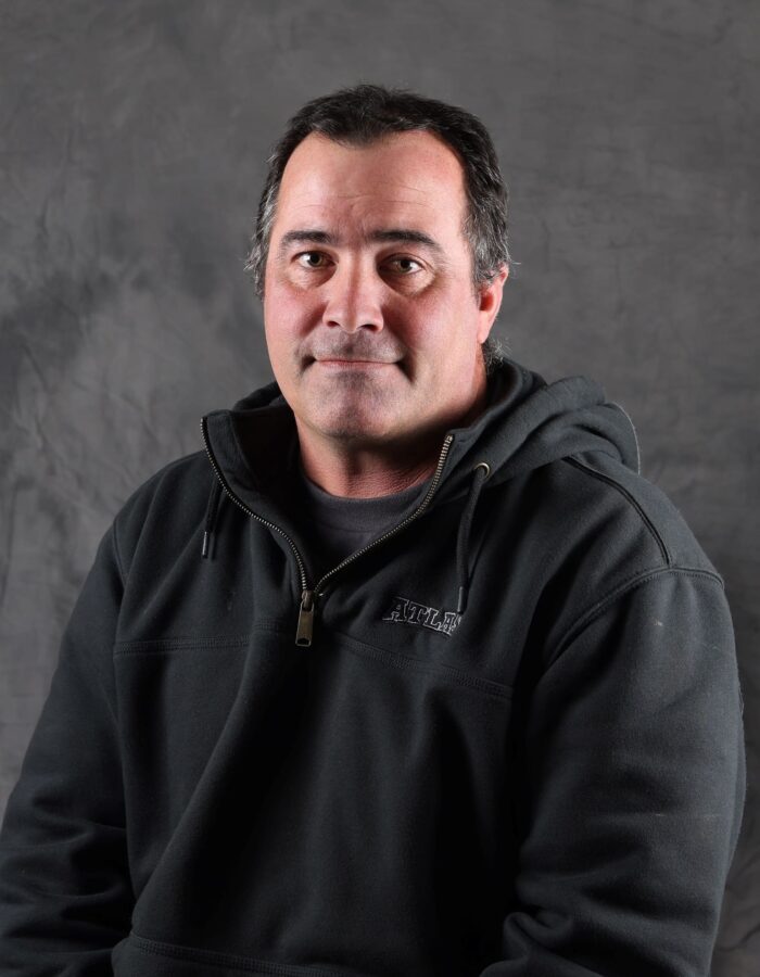 Man with short dark hair in black hoodie, gray backdrop.