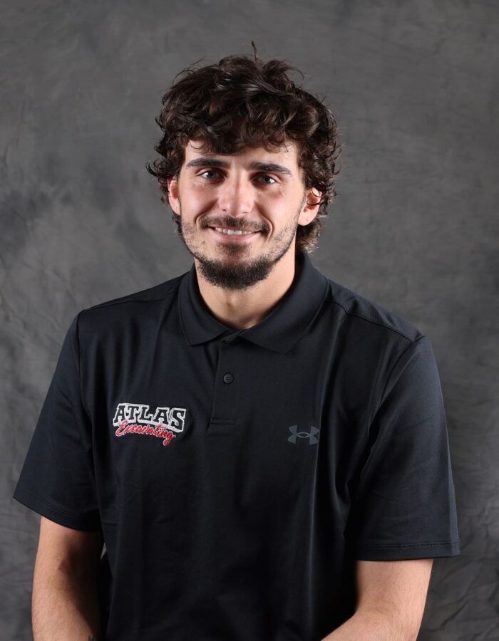 Smiling man with curly hair and beard in black polo.
