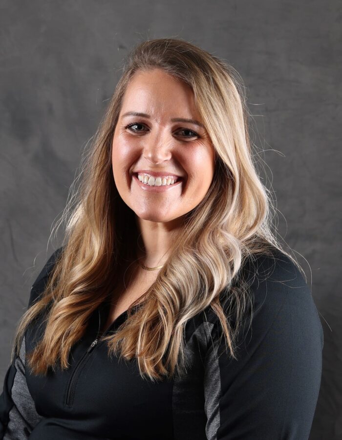 Smiling blonde woman in black top against gray background.