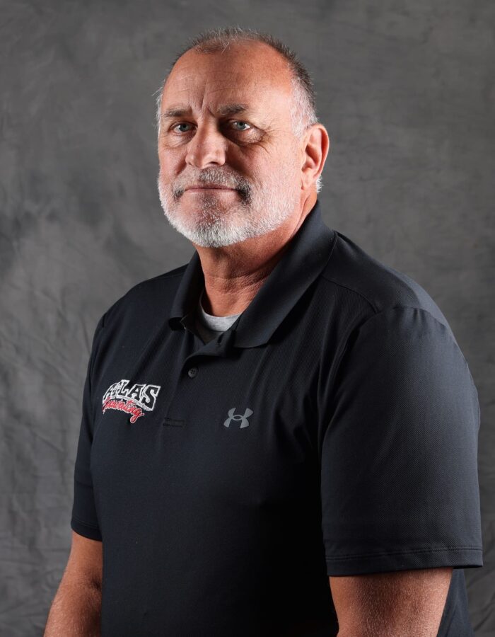 Gray-haired, bearded man in black polo on gray backdrop.