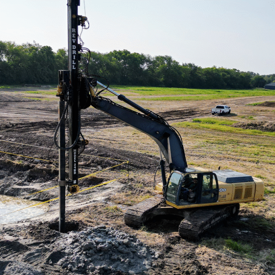 Excavator drill works on site; white pickup in background.
