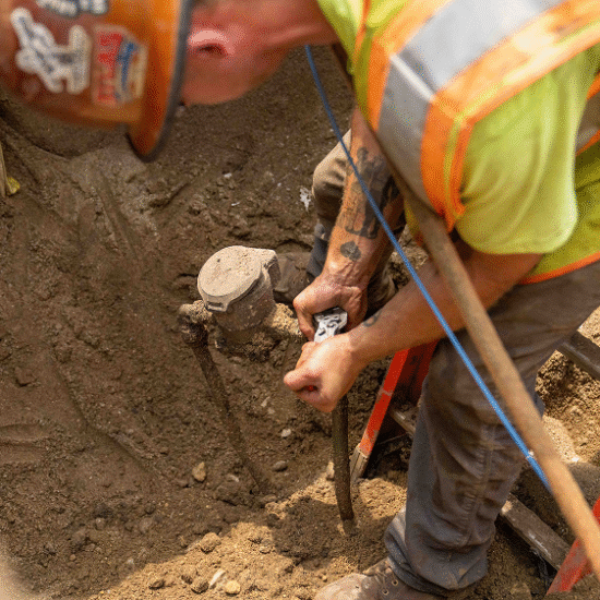 Worker in hard hat fixing underground pipe amid dirt.