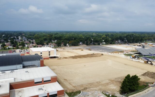 Aerial view: construction site, machinery, school, fields, stadium.