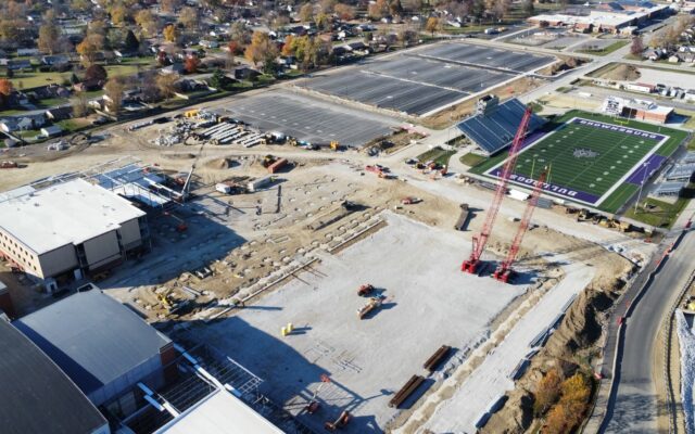 Aerial view: construction site beside school field and parking lot.