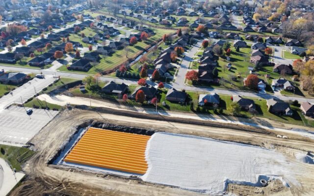 Aerial view: orange pipes in construction pit near suburban homes.