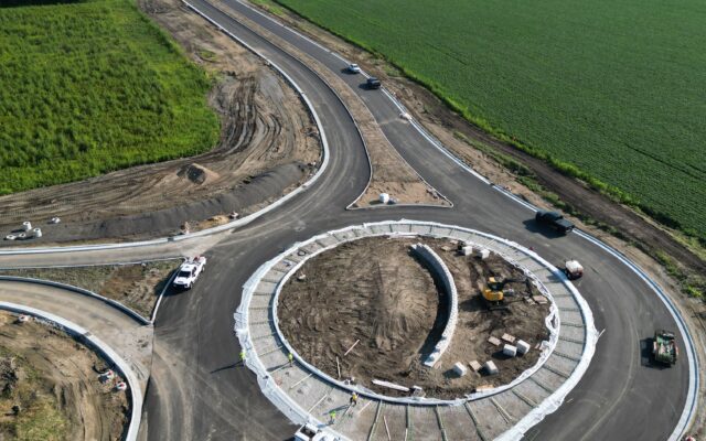 Aerial view of roundabout construction amid farmland and vehicles.