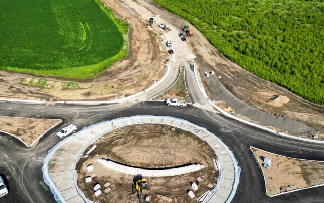 Aerial view of roundabout construction with vehicles, green fields.