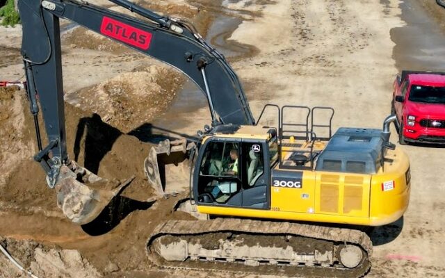 ATLAS yellow and black excavator lifts soil at construction site.