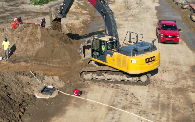 Excavator and workers on a partially paved road construction site.