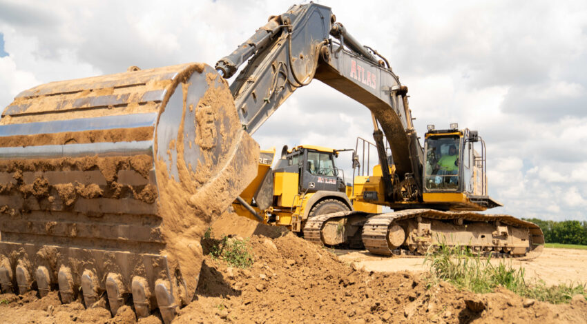 Two yellow excavators dig and move soil at construction site.