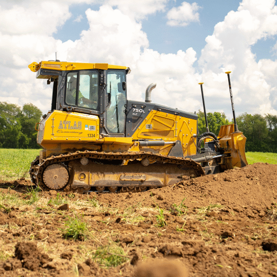 Yellow ATLAS bulldozer pushes dirt in grassy field.