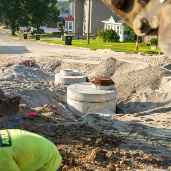 Worker in green shirt at construction site with pipes and sand.
